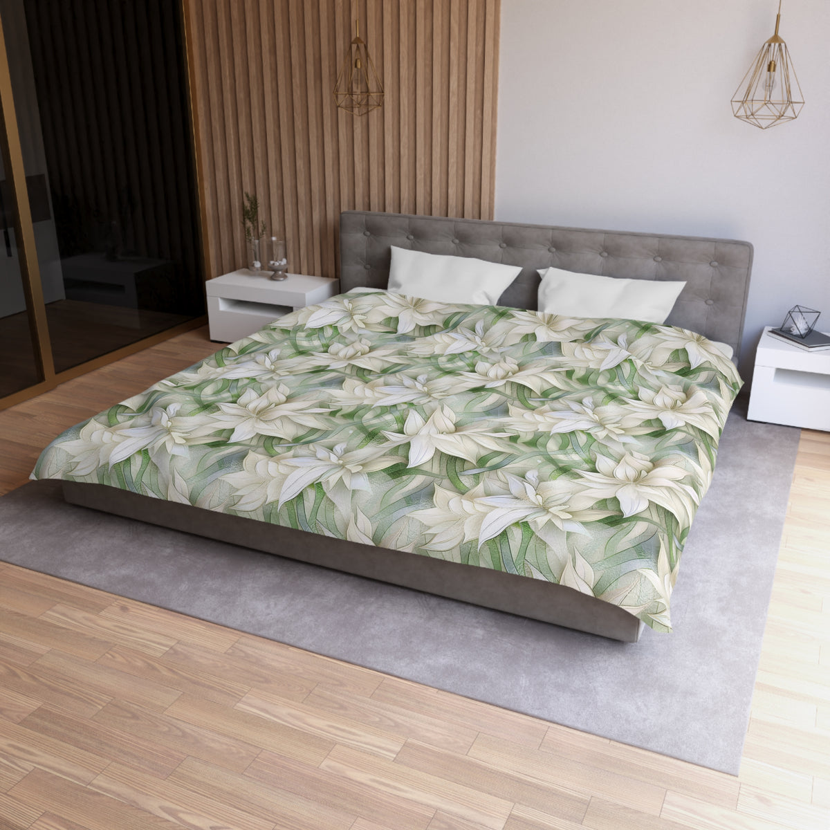 a modern bedroom with a large bed covered in a floral print comforter. The bed is positioned against a wall with a wooden panel. The room has a minimalist design, with a gray headboard and white nightstands. There is a pendant light hanging above the bed, and a vase on one of the nightstands. The overall color scheme of the room is neutral, with the floral print adding a touch of nature and color.