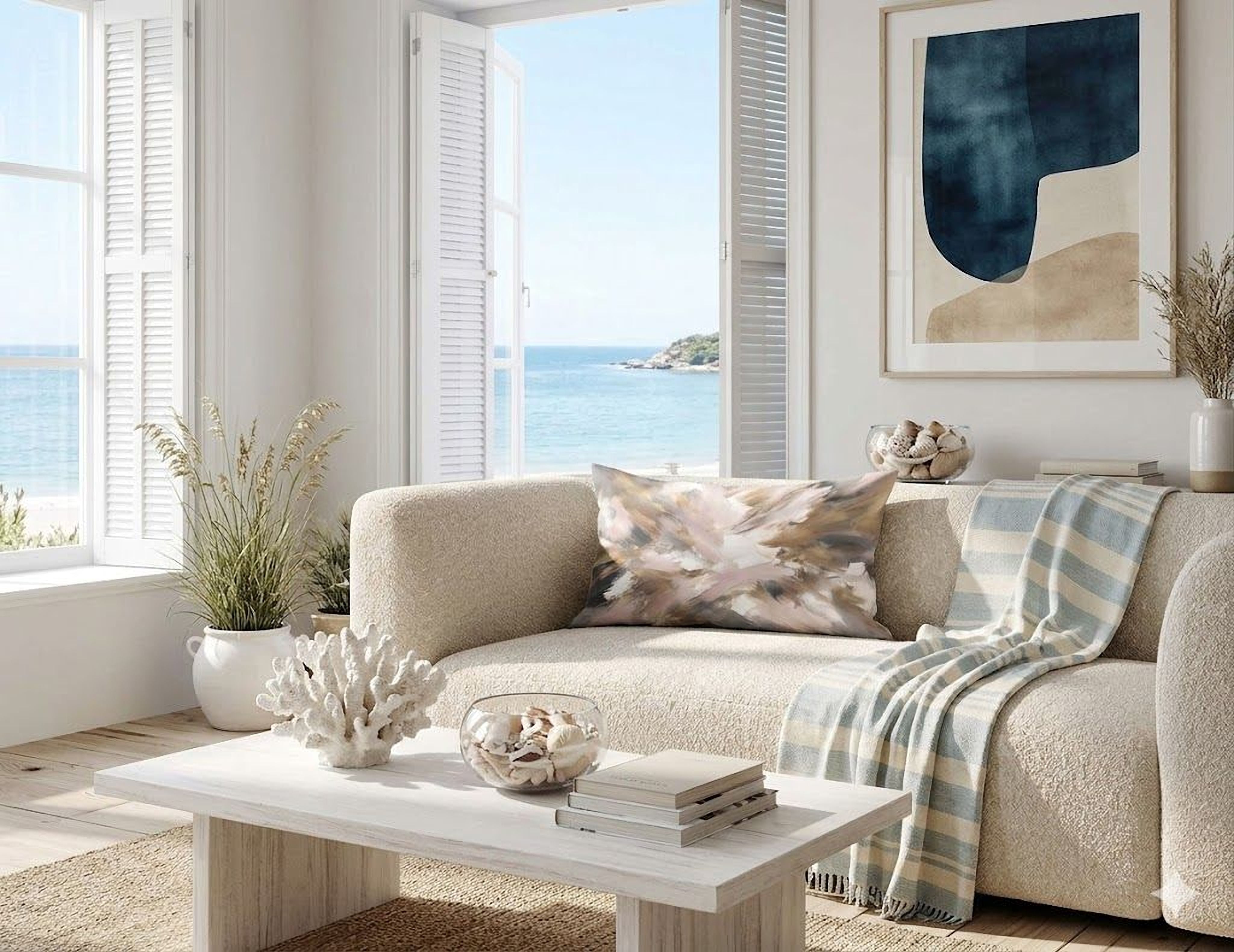 a cozy living room with a large window overlooking the ocean, providing a serene view. The room is decorated with a beige sofa, a white coffee table, and various decorative items such as a vase, a plant, and a painting. The overall atmosphere of the room is calm and inviting, with the ocean view adding a sense of tranquility and natural beauty.