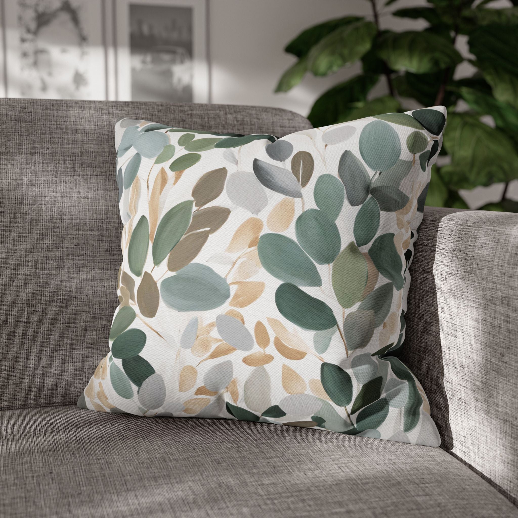 A gray couch with a decorative throw pillow featuring a leaf pattern in shades of green, brown, and gray.