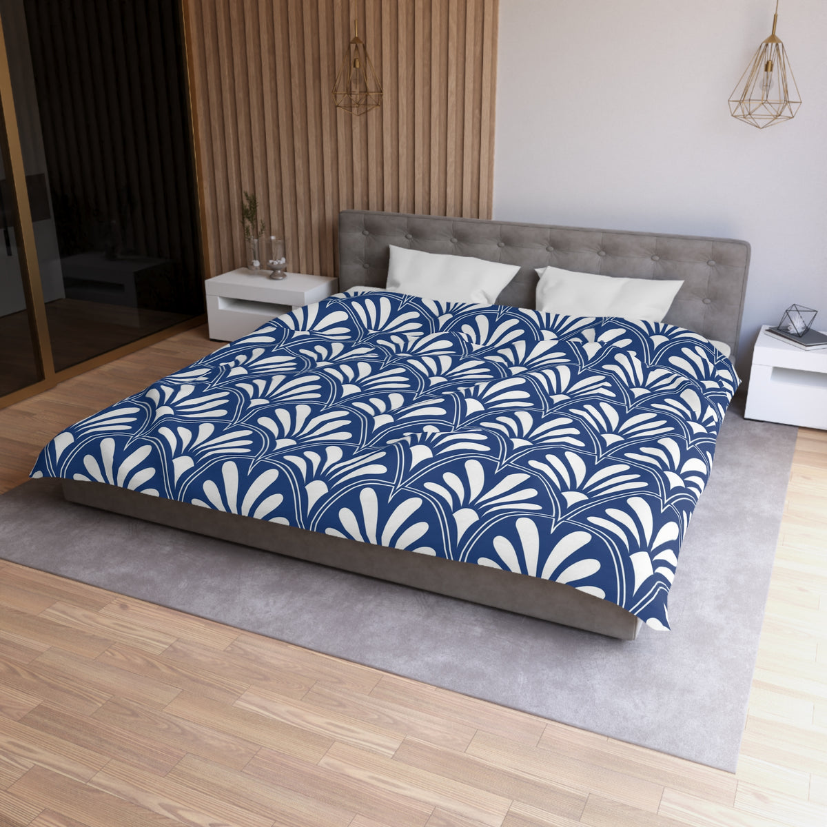 a modern bedroom with a large bed featuring a blue and white patterned comforter. The bed is positioned against a wall with a wooden panel, and there are two nightstands on either side of the bed. The room has a minimalist and clean design, with a gray headboard and a wooden floor.