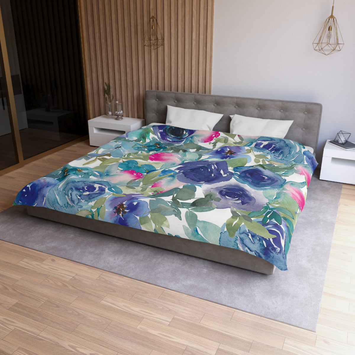a bedroom with a large bed covered in a colorful floral comforter. The bed is positioned against a wall with a wooden panel. The room has a modern and minimalist design, with a gray headboard and white nightstands.