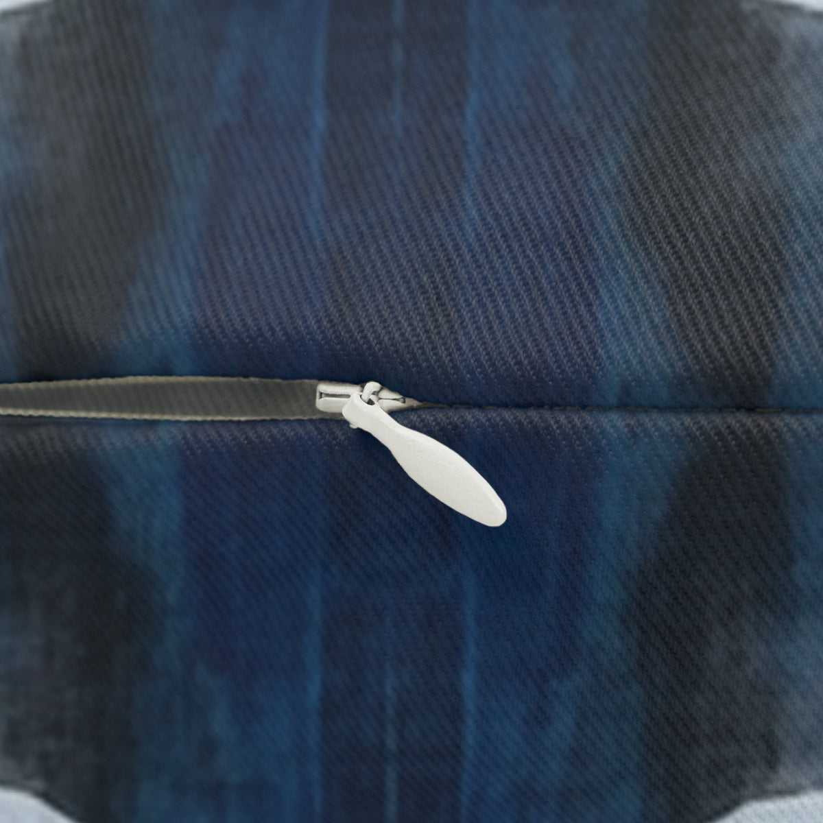 A close-up view of a zipper on a blue and black fabric, with a white plastic zipper pull visible.