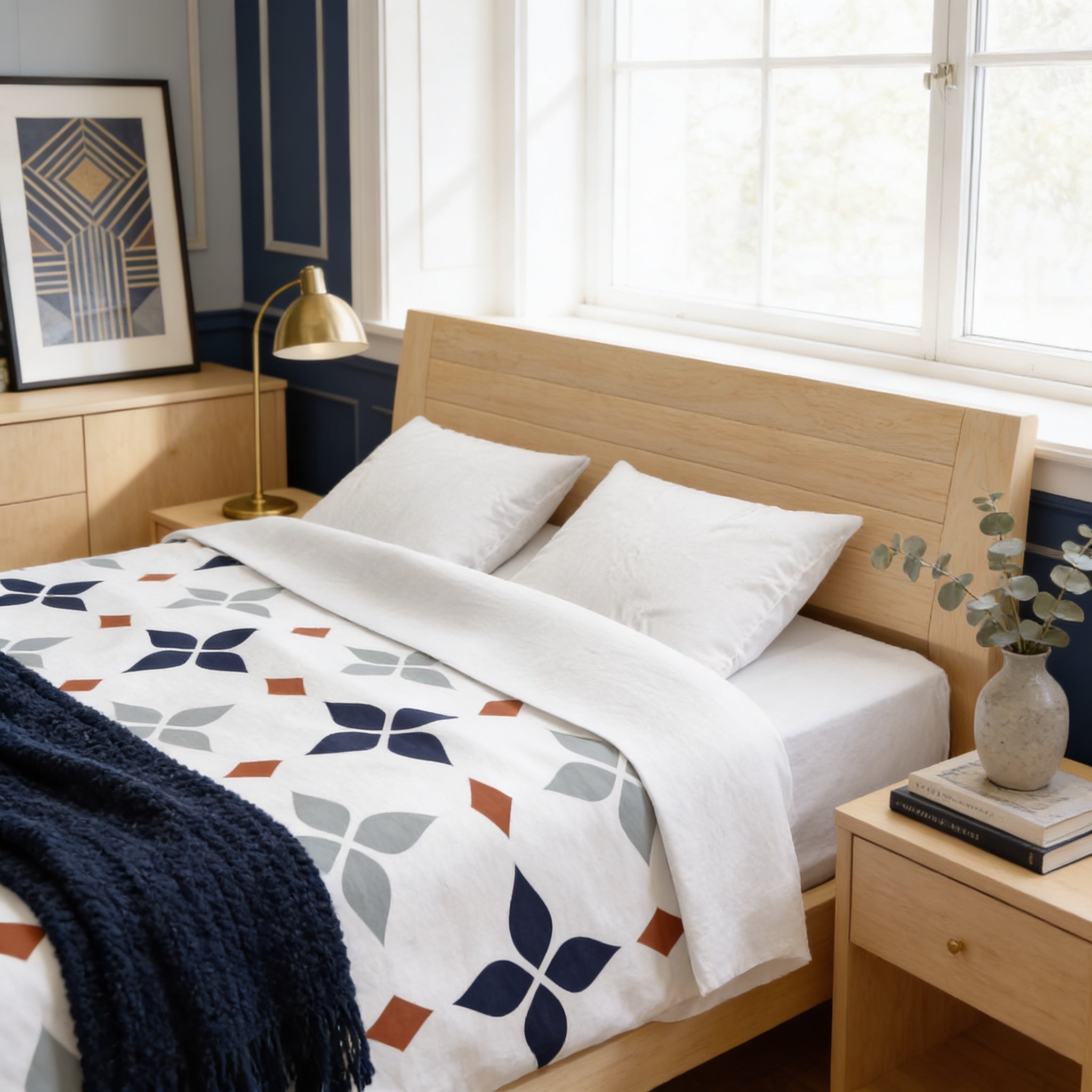 a cozy bedroom with a wooden bed frame, a white and blue patterned comforter, and a wooden nightstand with a lamp. The room has a window that allows natural light to enter, and there is a framed picture on the wall.