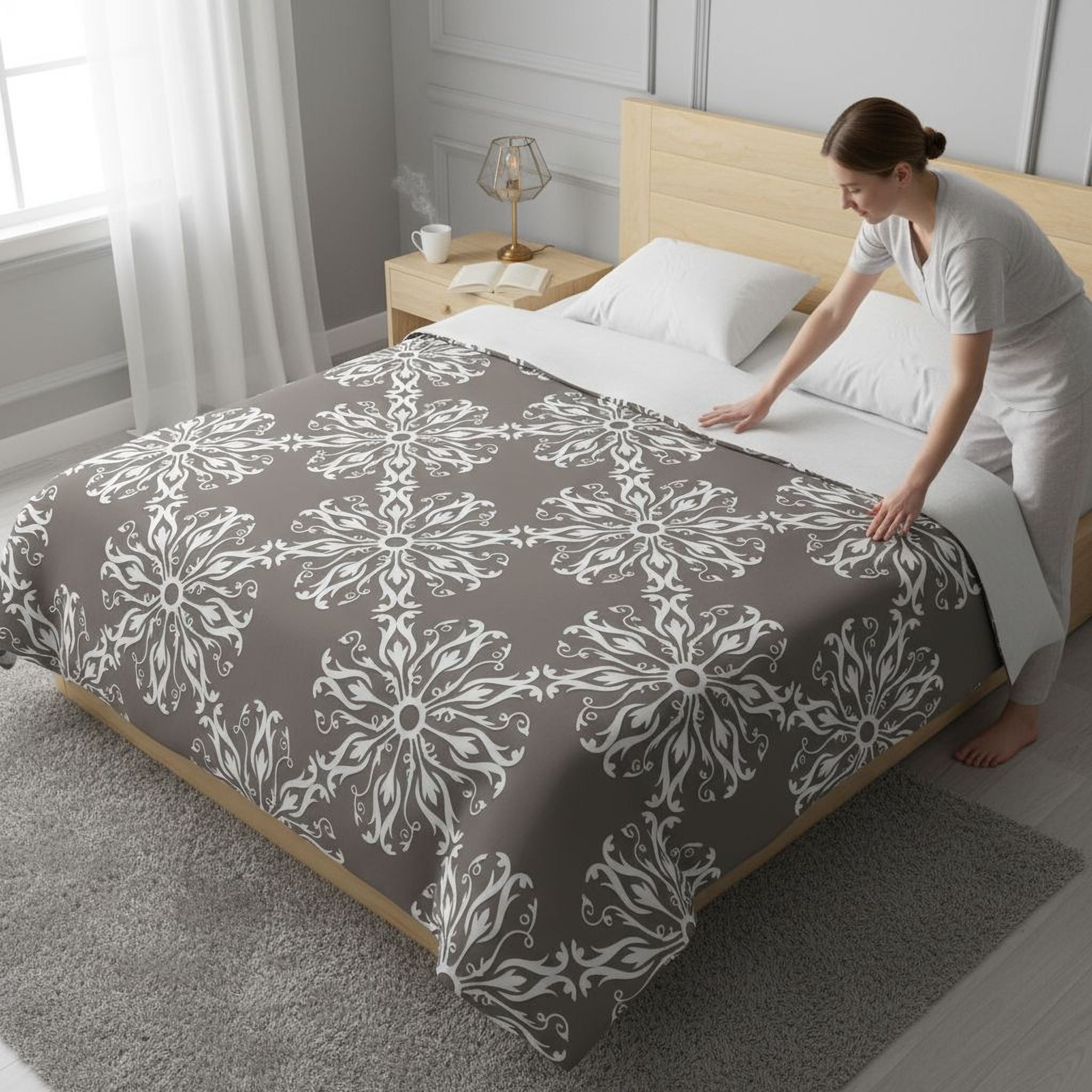 A woman is making the bed in a bedroom with a gray and white patterned bedspread.