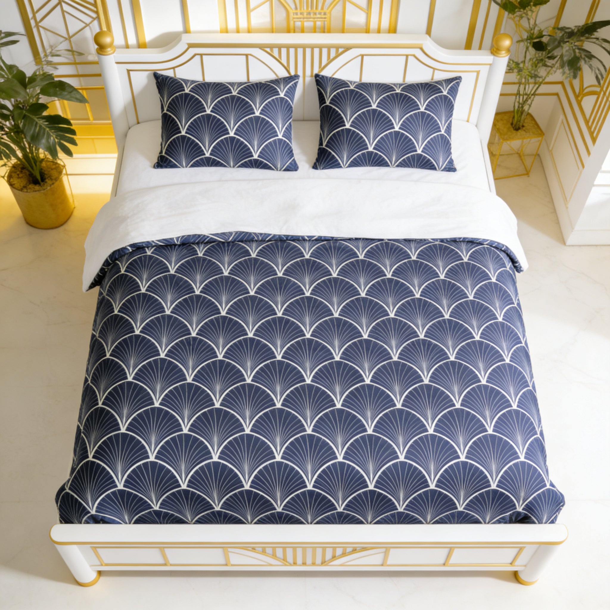 a bedroom with a white bed frame and a blue and white patterned comforter. The bed is neatly made with a white sheet and two matching pillows. The room has a gold-framed mirror on the wall, and there are some plants in the room, adding a touch of greenery to the space.