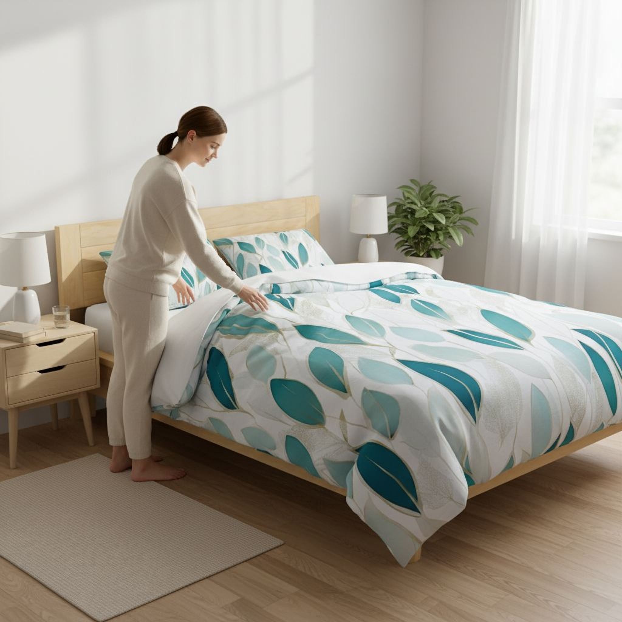 A woman in a beige outfit is arranging the bed with a leaf-patterned comforter and pillows in a bright, well-lit bedroom.