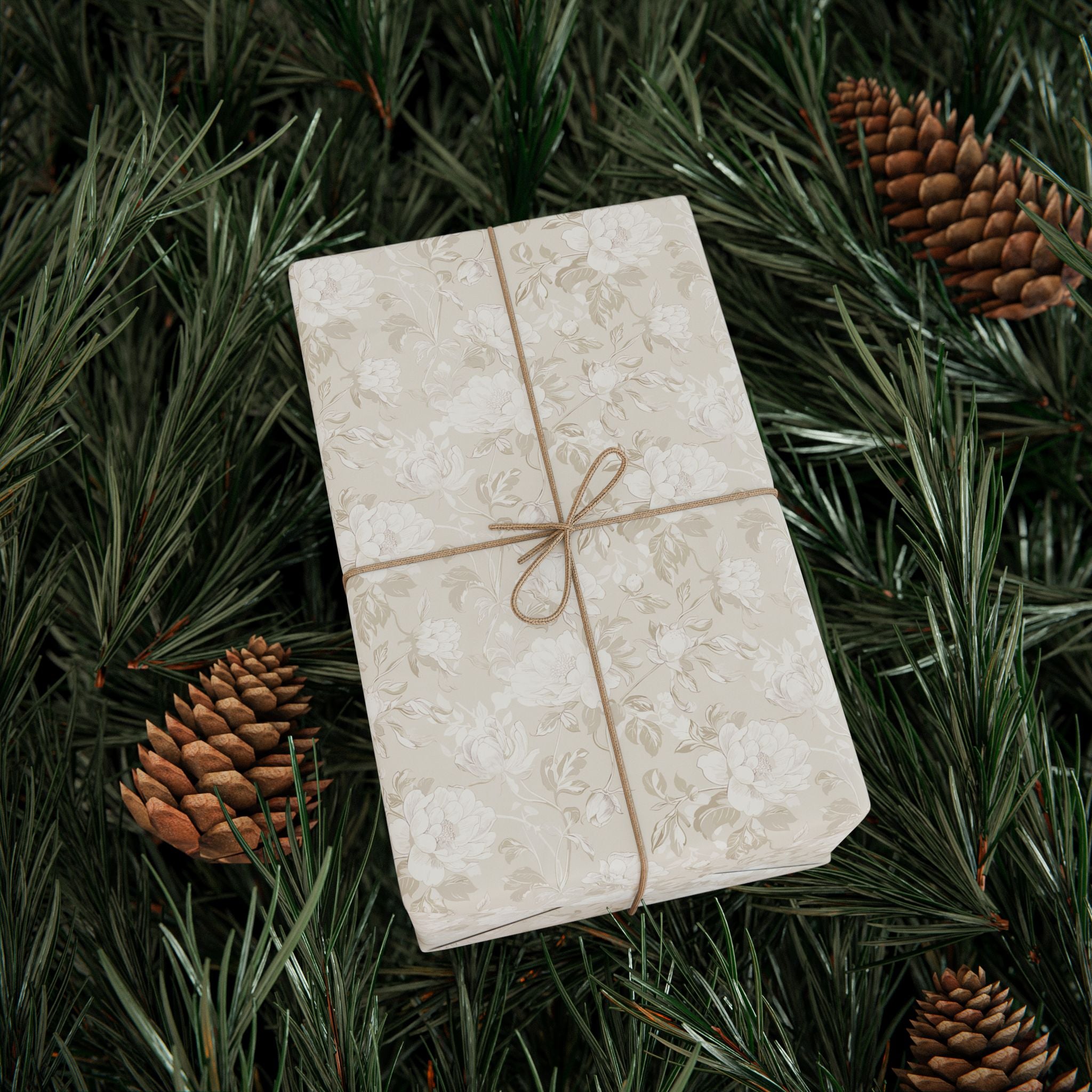 A white gift box with a floral pattern is surrounded by pine needles and pine cones, creating a festive and natural setting.