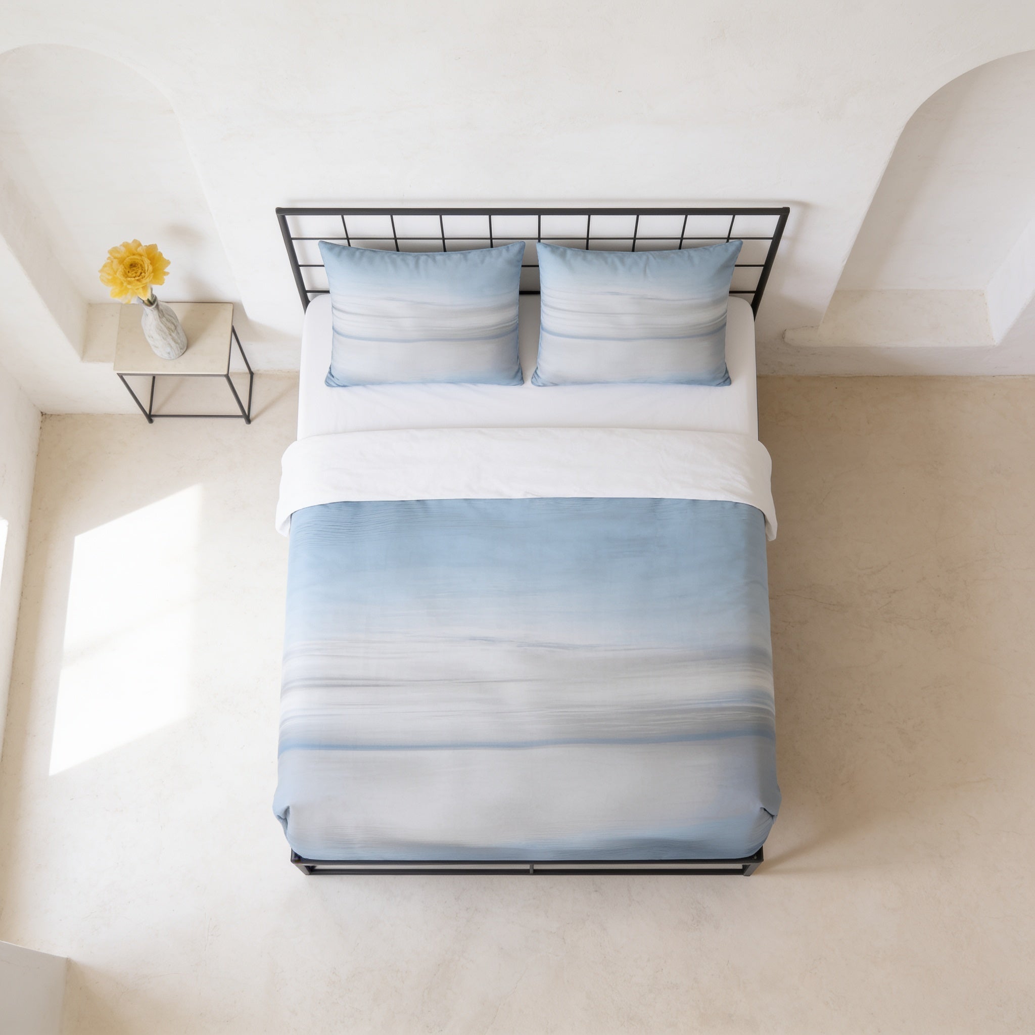 a neatly made bed with a blue and white striped comforter and matching pillows, placed in a room with white walls and a minimalist design.