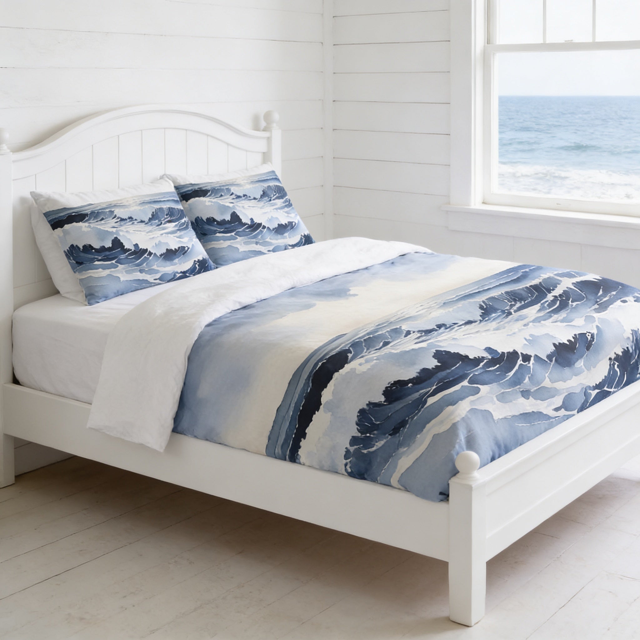 a white wooden bed with a blue and white ocean-themed comforter and pillows, positioned in front of a window overlooking the ocean.