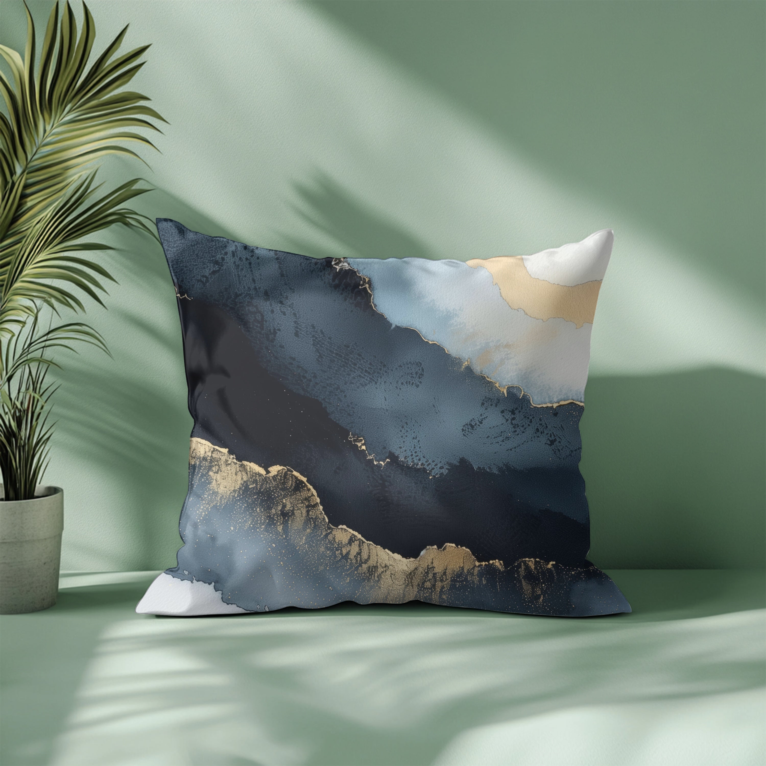 a decorative pillow with a striking abstract design, including blue, white, and gold colors, placed on a green surface next to a potted plant.