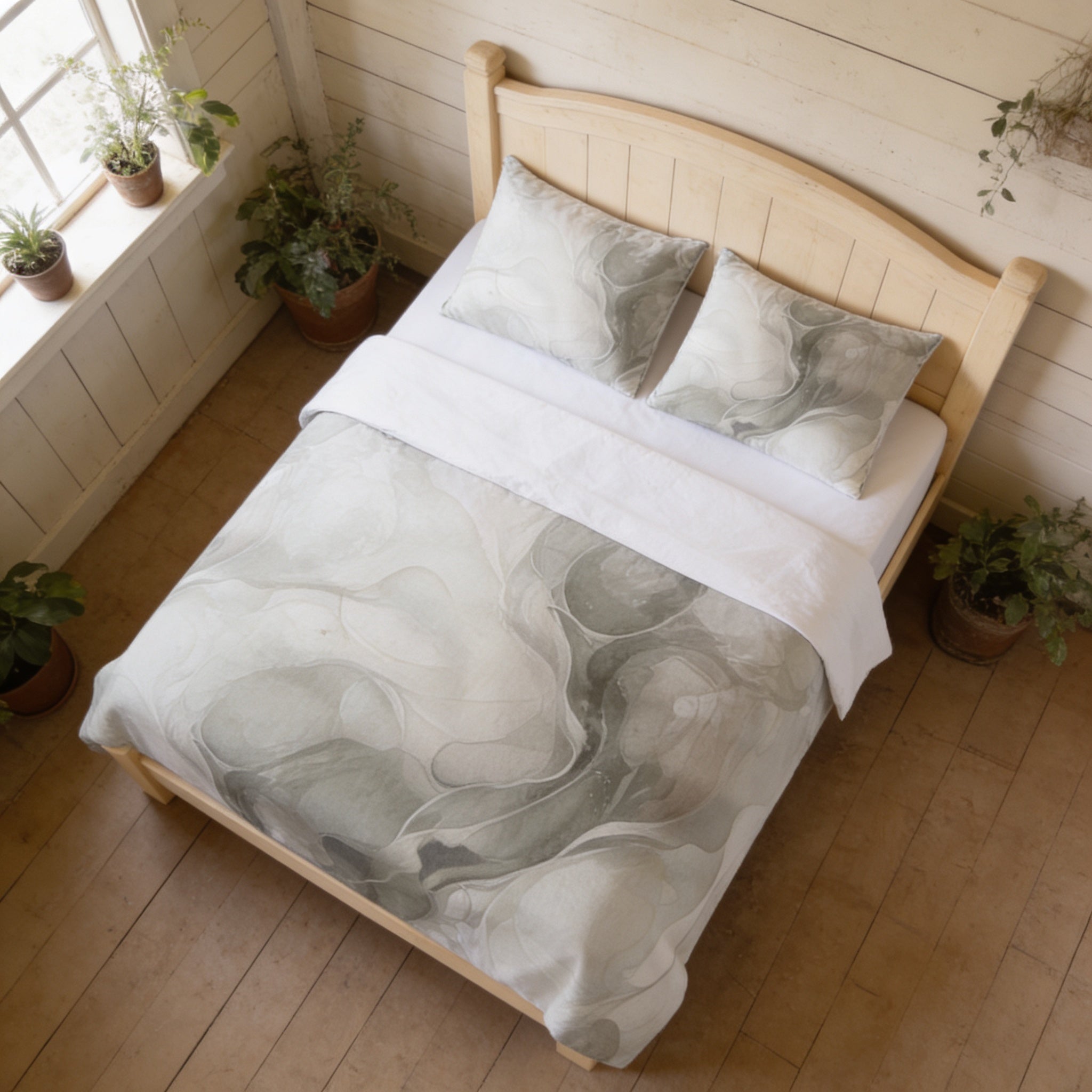 a cozy bedroom with a wooden bed frame, a white comforter with a gray and white abstract pattern, and two matching pillows. The room has a warm, inviting atmosphere, with potted plants placed around the bed and a window providing natural light.