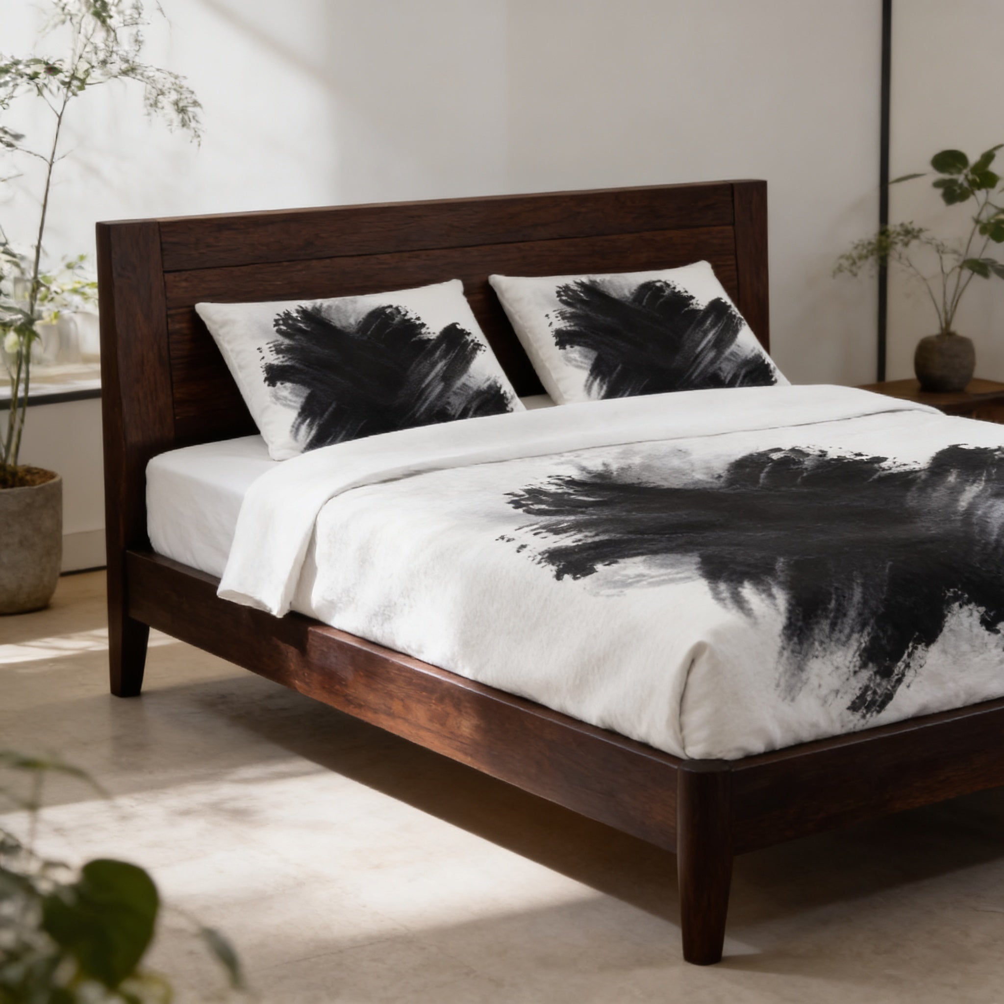 a modern bedroom with a wooden bed frame and a white comforter with black brushstrokes on it. The bed is positioned against a white wall, and there are two potted plants in the room.