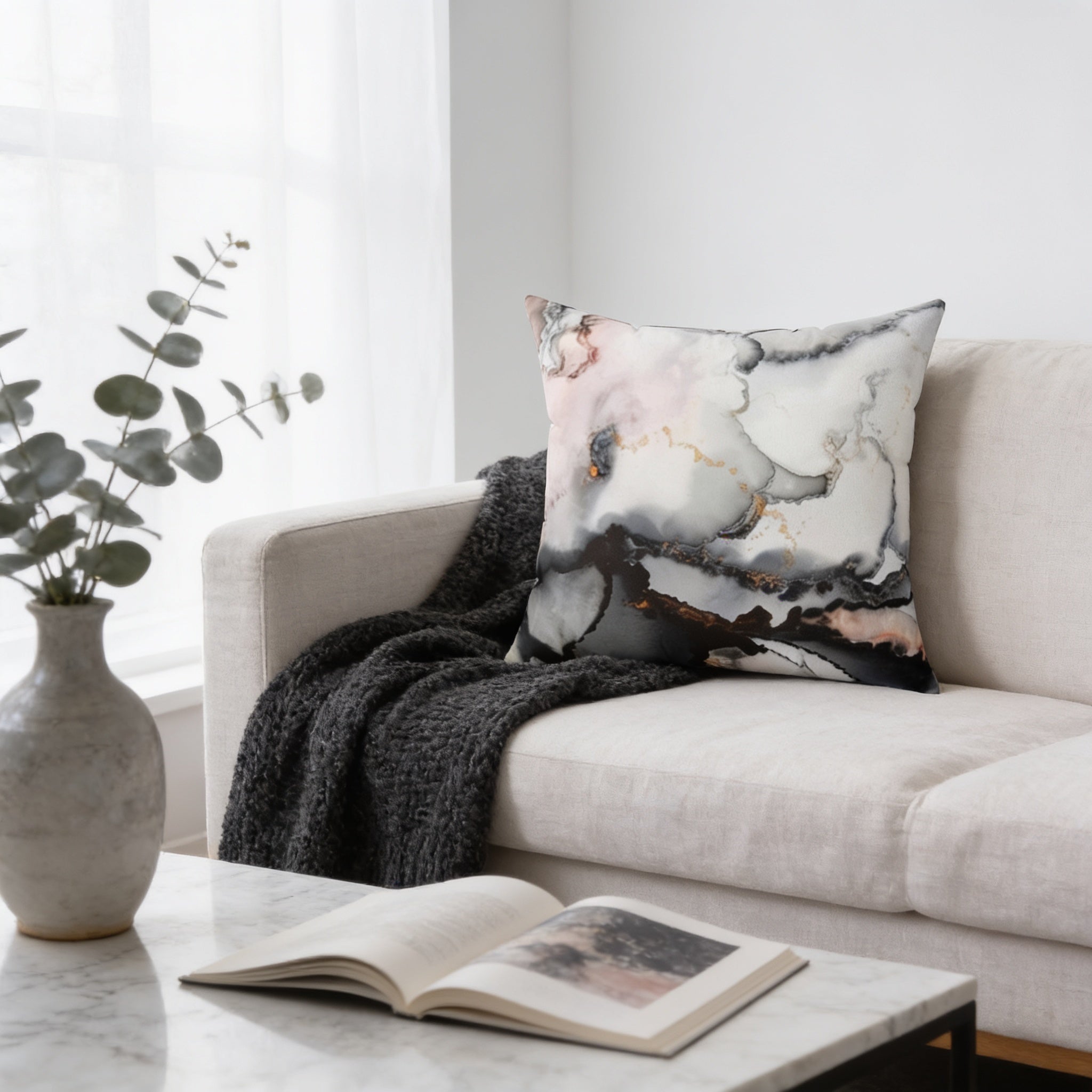 a cozy living room with a white sofa, a gray blanket, a white vase with greenery, and an open book on a marble coffee table.