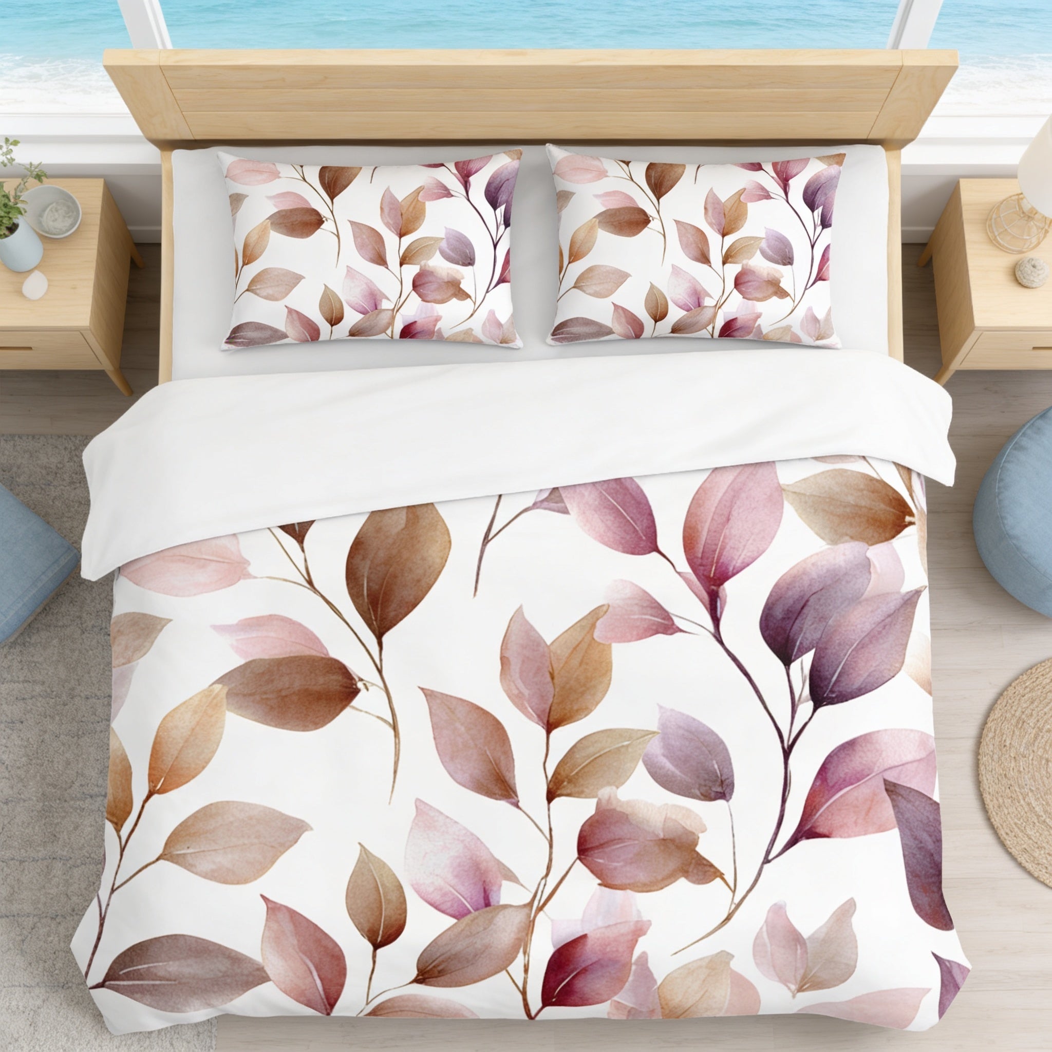 a bedroom with a bed featuring a white comforter and pillows decorated with a leaf pattern in shades of pink and brown. The bed is positioned next to a window overlooking the ocean, creating a serene and relaxing atmosphere.