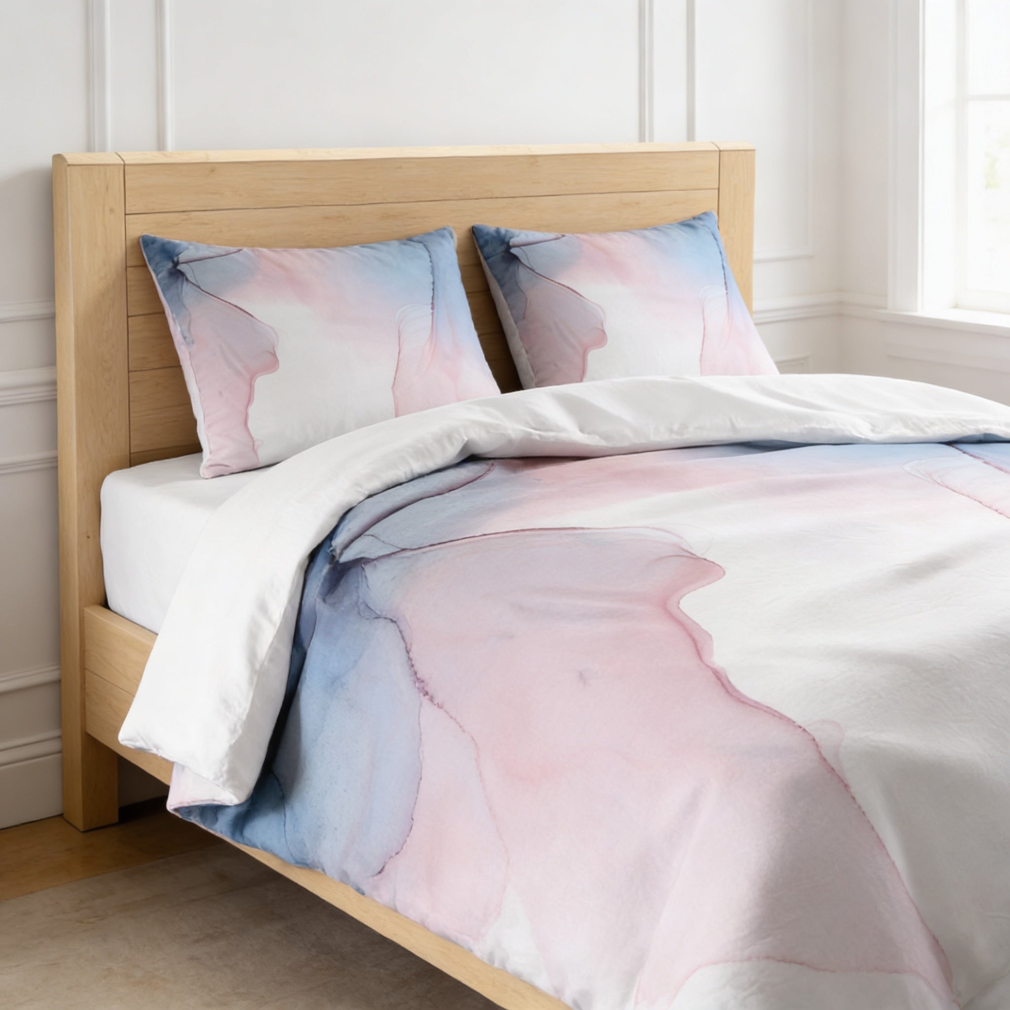 a bed with a white and blue watercolor-style comforter and pillows, set against a white wall and wooden headboard.