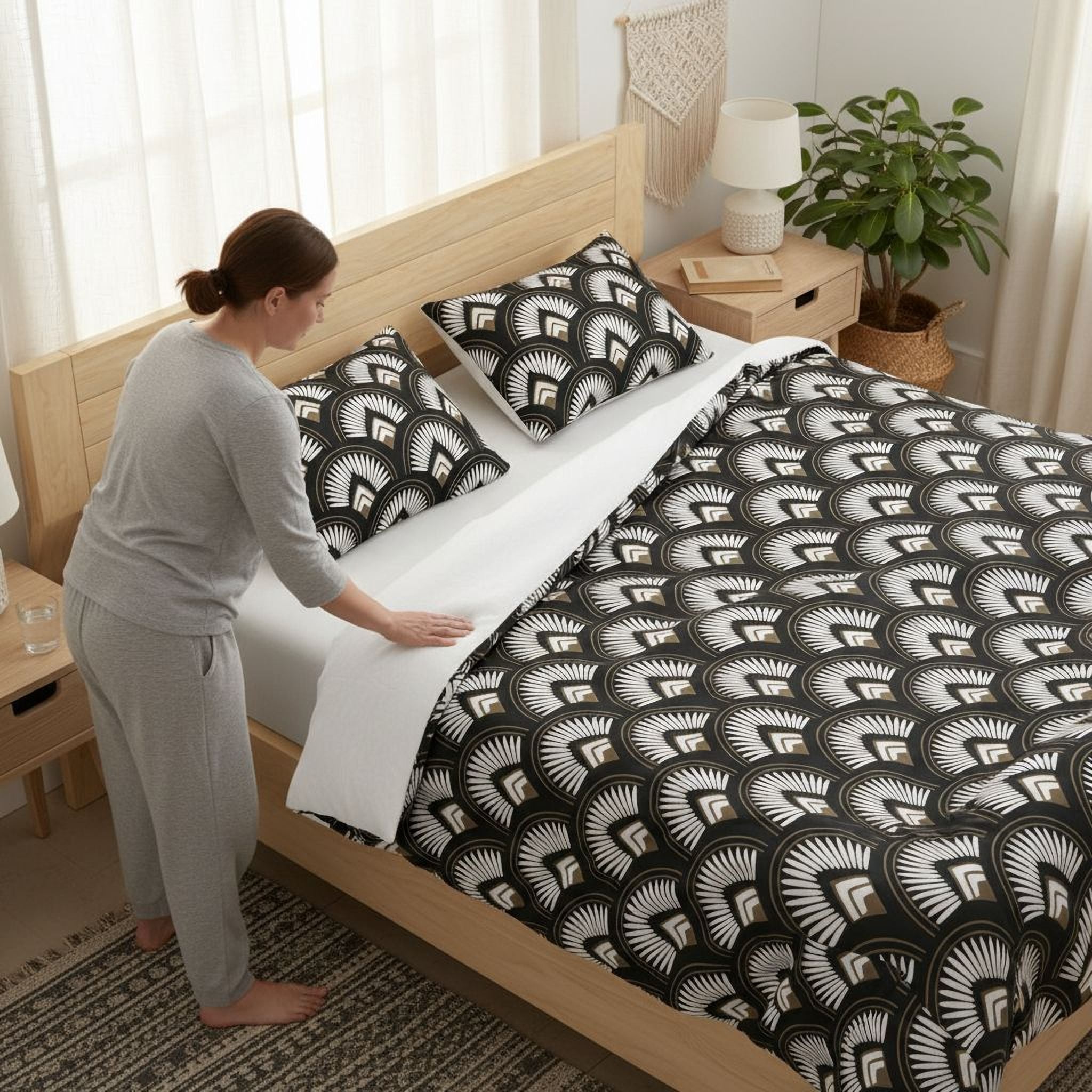 A woman in a gray outfit is arranging the bed with a black and white patterned comforter and pillows.