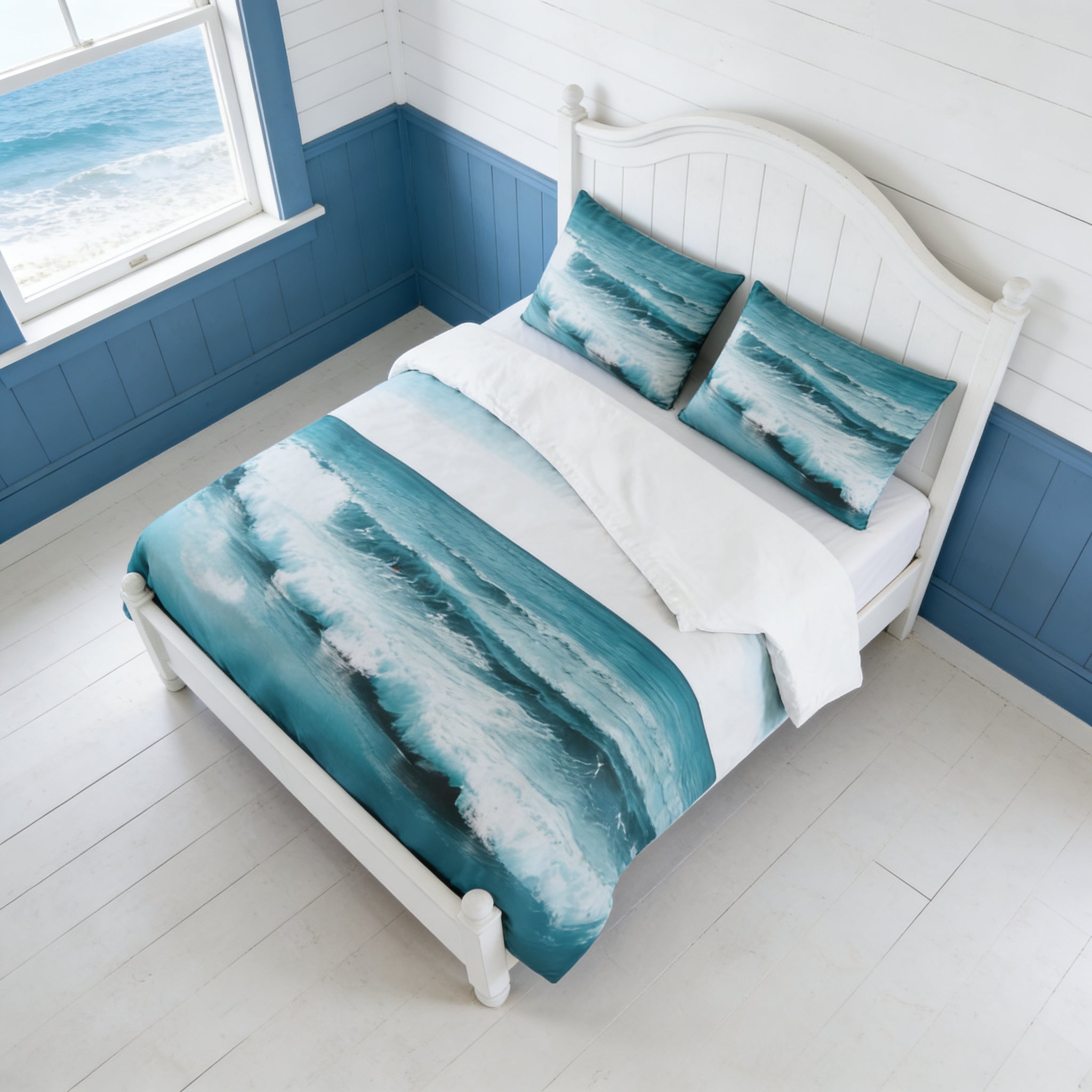 a bedroom with a white wooden bed frame and a white headboard. The bed is covered with a comforter featuring a wave pattern in shades of blue and white. The room has a window overlooking the ocean, creating a serene and calming atmosphere.