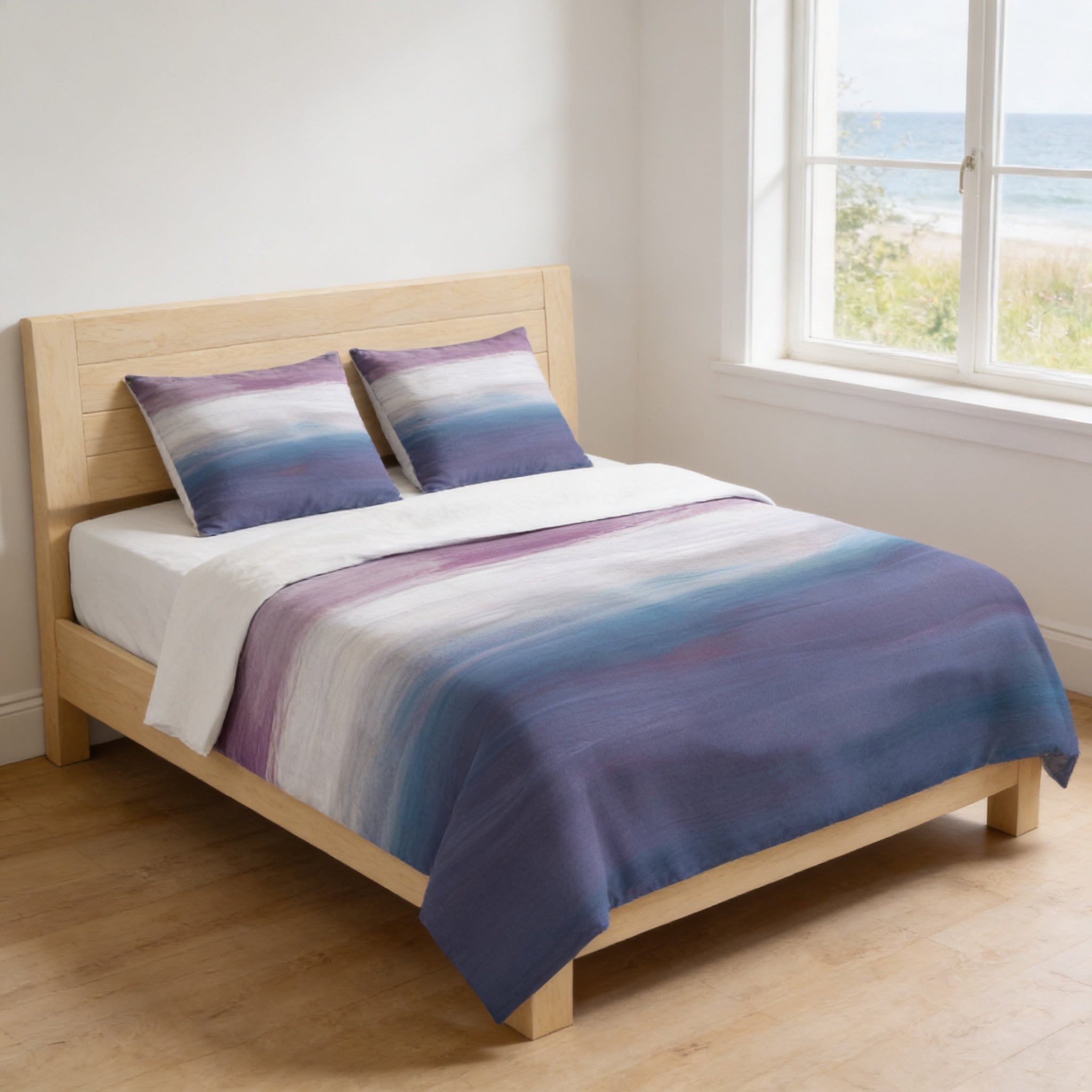 A cozy bedroom with a wooden bed frame, featuring a colorful duvet cover with a gradient of purple and blue hues. The bed is positioned against a wall with a window overlooking a scenic view of the ocean.