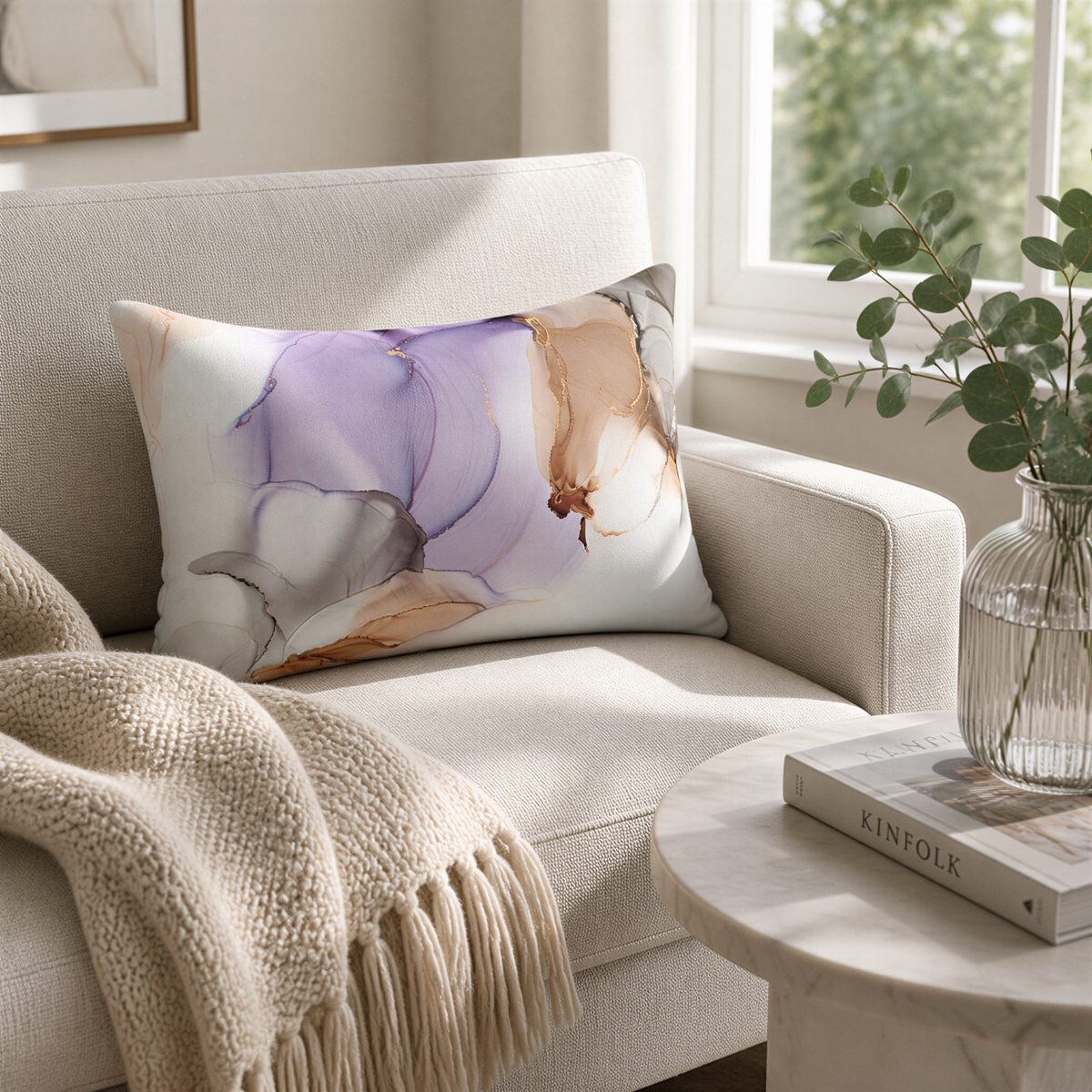 a cozy living room with a beige sofa, a white throw blanket, and a round table with a book and a vase of greenery.