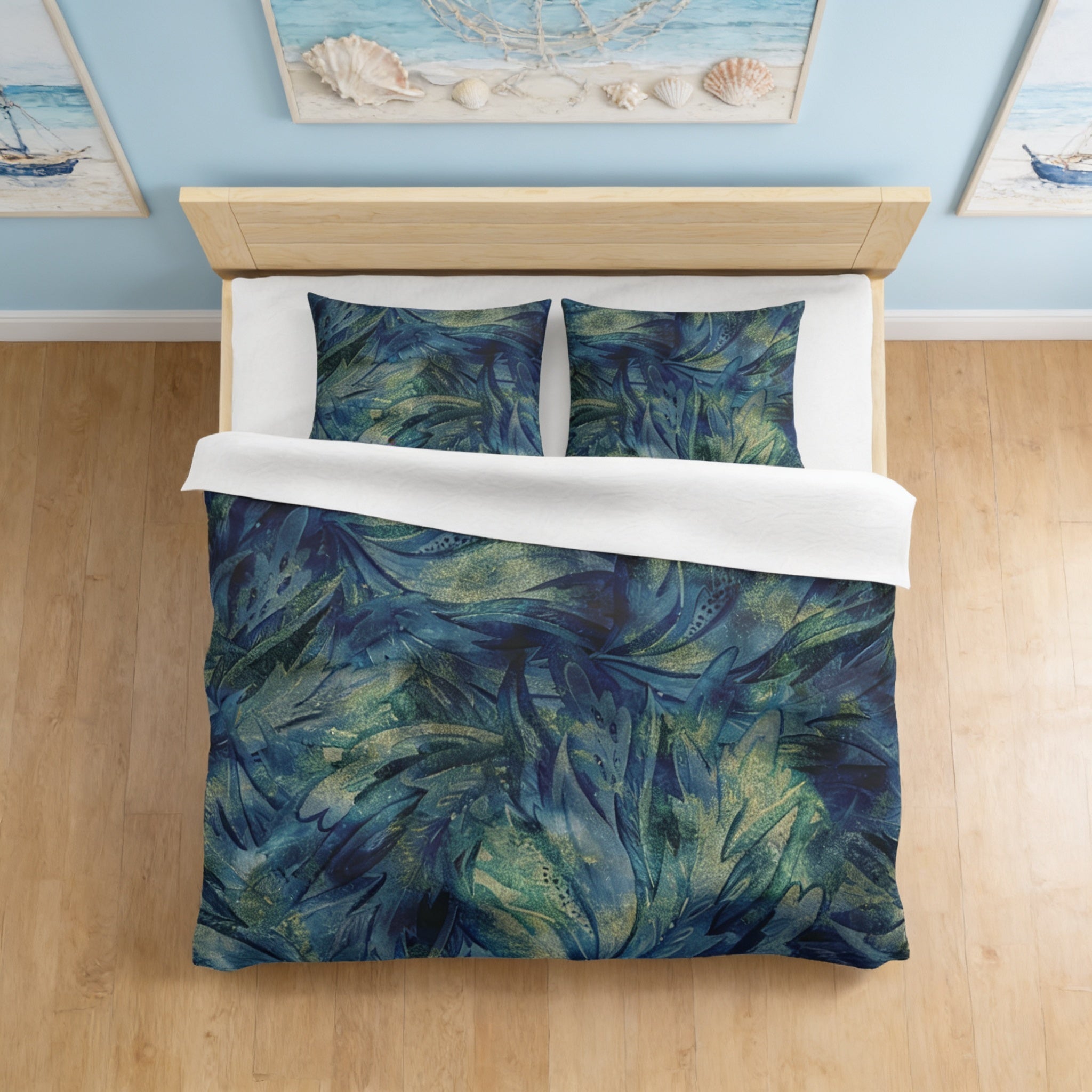 a bedroom with a bed covered in a blue and green leafy patterned comforter and pillows. The bed is set against a wall with framed pictures, creating a cozy and personalized atmosphere.