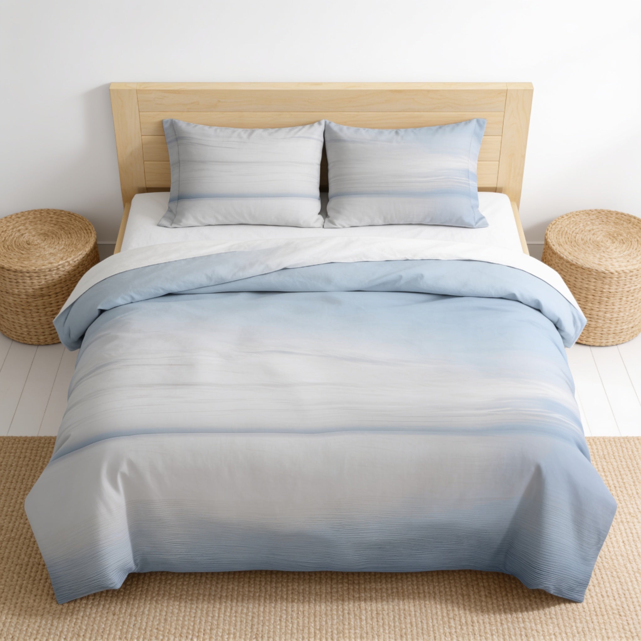 a neatly made bed with a blue and white gradient comforter and matching pillows. The bed is set against a white wall, and there are two round wicker side tables on either side of the bed.