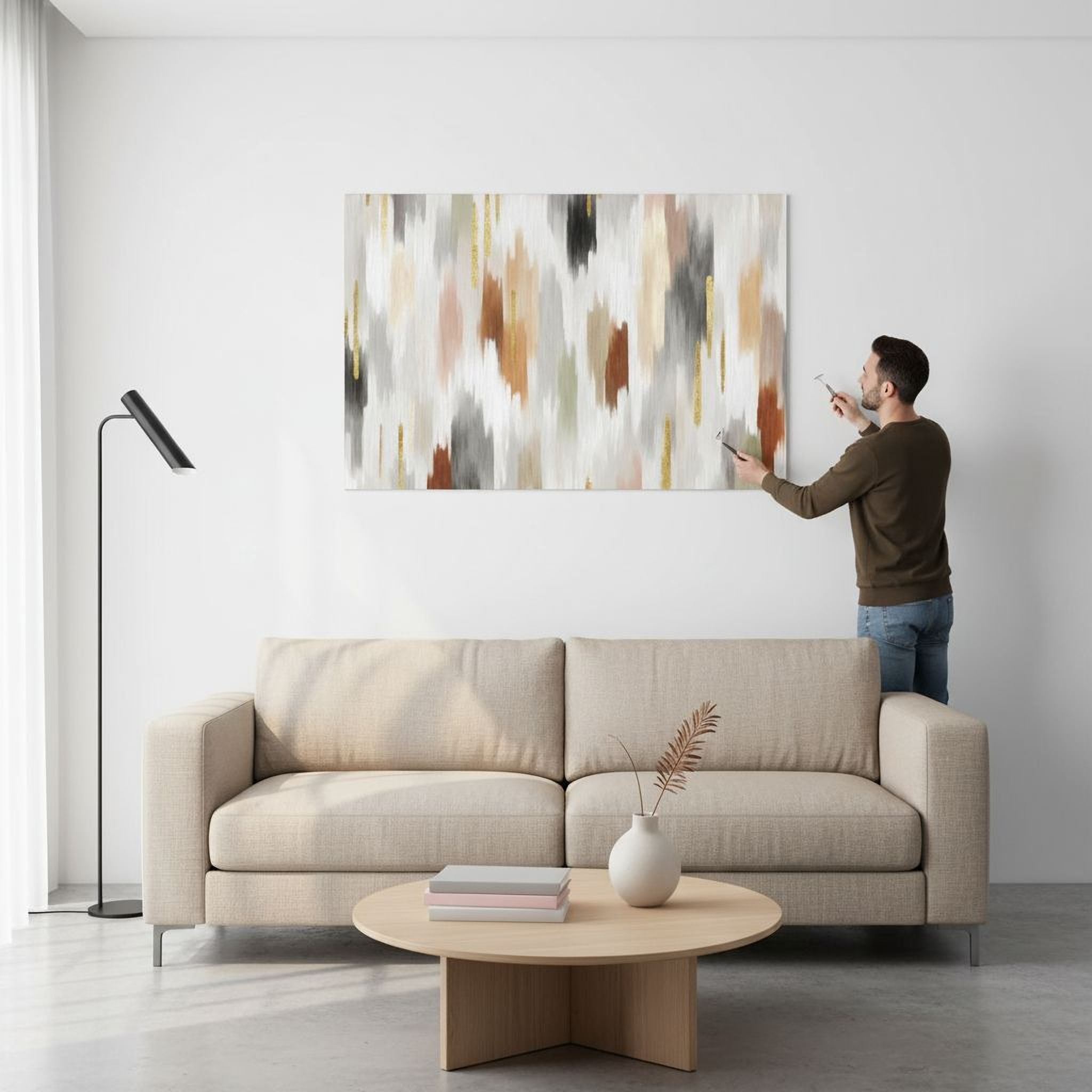 A man is standing in a living room, painting a large abstract artwork on the wall above a beige sofa.