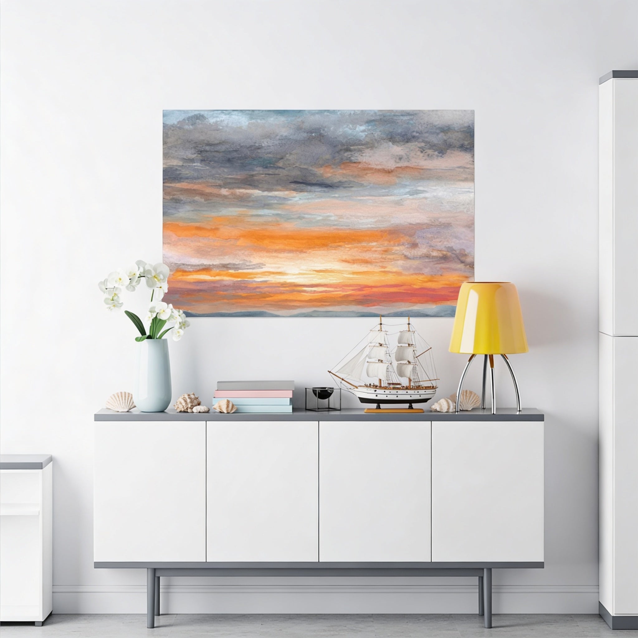 a white cabinet with a painting of a sunset on the wall above it, along with a vase of white flowers, a small model ship, and a yellow lamp on the cabinet.