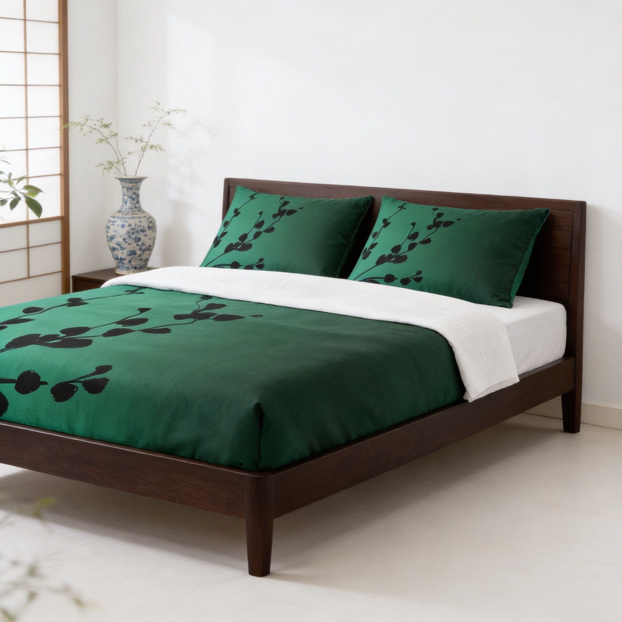 a modern bedroom with a wooden bed frame and a green comforter with black leaf patterns. The bed is set against a white wall, and there is a vase with flowers on the nightstand next to the bed.