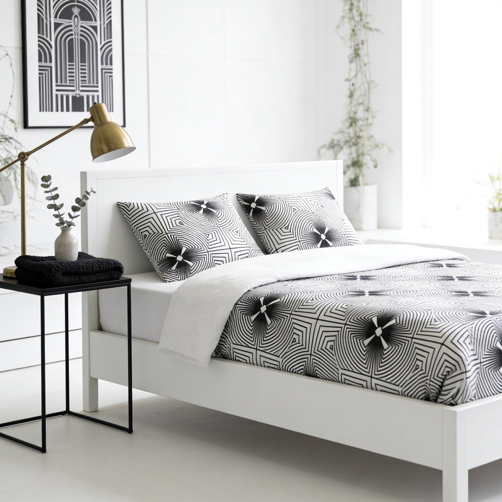 a modern bedroom with a white bed frame, a black and white patterned comforter, and a black nightstand with a lamp. The room has a minimalist and clean design, with white walls and a white floor.