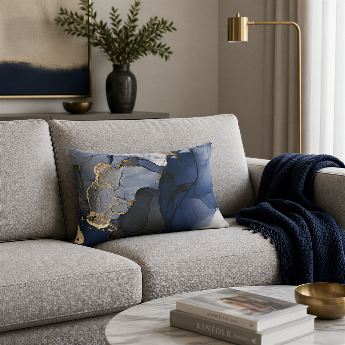 a living room with a gray sofa, a blue and white patterned throw pillow, a gold floor lamp, a marble coffee table, and a framed artwork on the wall.